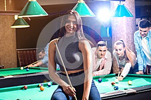 Young woman playing in billiard. Posing near the table with a cue in her hands