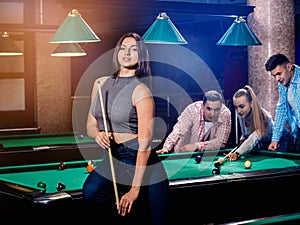 Young woman playing in billiard. Posing near the table with a cue in her hands