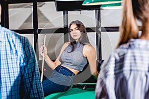 Young woman playing in billiard. Posing near the table with a cue in her hands