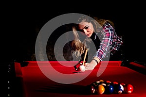 Young woman playing billiards in the dark billiard club