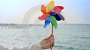 Young woman playing with a colorful spinning pinwheel on the sandy sea beach. Summer holiday, travel, and positive emotions
