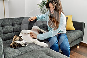 Young woman playing with dog sitting on sofa at home