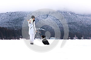 Young woman playing with dog in snow, playing fetch, winter wonderland, pet owner.
