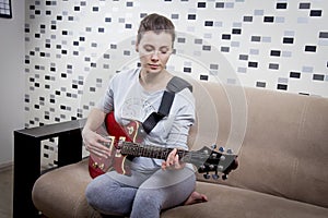 Young woman is playing electric guitar at home. The girl is musician