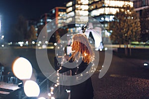 Young woman playing with fairy lights in city at winter