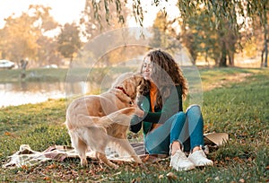 Young woman playing with her dog golden retriever at the autumn park