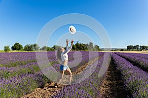 A young woman playing with her hat in a blooming lavender field.