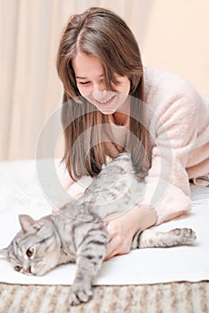 young woman playing with her tabby cat lying on a bed. stroking pet gently, friendship and love.