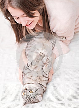 young woman playing with her tabby cat lying on a bed. stroking pet gently, friendship and love. vertical shot.