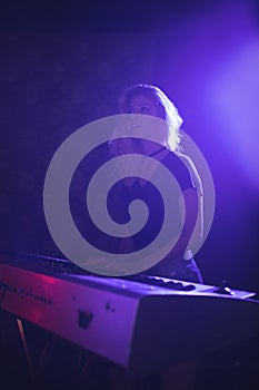 Young woman playing piano on illuminated stage in nightclub