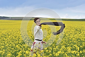Young woman playing with scarf in a canola field