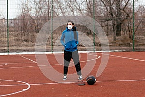 A young woman is playing sports on a sports field in a mask. Protection from coronavirus infection with a medical mask