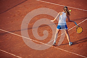 Young woman playing tennis on clay. Forehand.