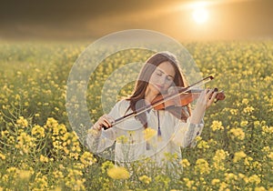 Young woman playing violin in a field at sunset