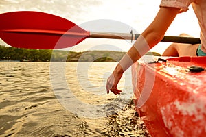 Young Woman Playing with Water while Sitting in Kayak on Beautiful River or Lake at Sunset. Close up of Female Hand.