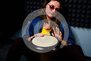 A young woman plays a drum djembe sitting on the floor in a recording Studio. Ethnic African percussion instrument Darbuka