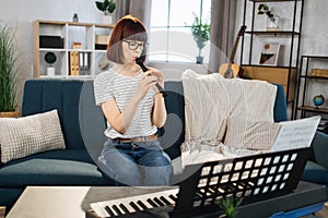 Young woman plays the flute on bright living room at home.
