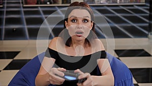 A young woman plays video games while sitting in an easy chair in the game room