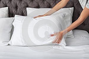 Young woman plumping white pillow on bed