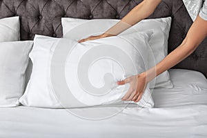 Young woman plumping white pillow on bed photo