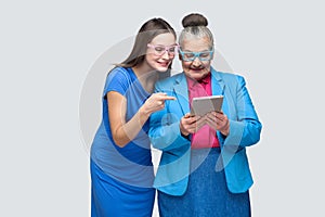 Young woman pointing finger at tablet in hands old woman