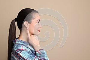 Young woman pointing at her ear on beige background. Space for text