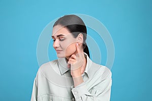 Young woman pointing at her ear on light blue background