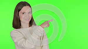 Young Woman Pointing on Side on Green Background