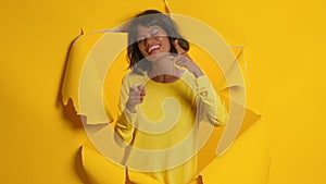 Young woman points at camera and says hey you picks someone, yellow background