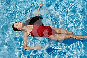 Young woman in the pool in a red swimsuit with a beautiful smile lying on the water and swimming in the sun swimming in