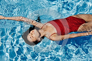 Young woman in the pool in a red swimsuit with a beautiful smile lying on the water and swimming in the sun swimming in