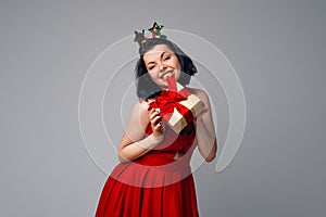 Young woman portrait hold gift in christmas color style, wearing red dress. Smiling happy girl on white background