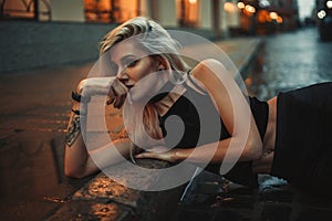 Young woman portrait lying on wet pavement on city street in eve photo