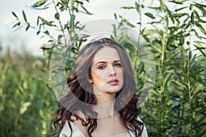 Young woman portrait. Perfect female face. Brunette girl with curly hair outdoors on green leaves background