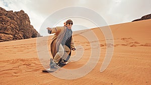 Young woman posing as sand dune surfing wearing bisht - traditional Bedouin coat. Sandsurfing is one of the attractions in Wadi photo