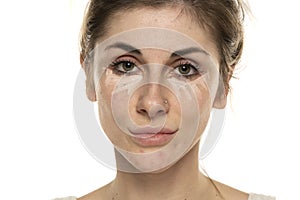 Young woman posing with concealer under her eyes on white background