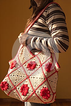 Young woman posing with a crocheted tote bag, with red flowers