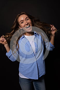 Young woman posing with happy smile. Hands throws hair. Black background