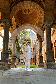 Young woman posing for photo in the arch of historic building. Full-length portrait of girl looking over her shoulder