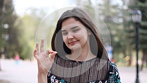 Young woman posing showing hand gesture ok on park background.