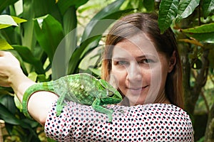 Young woman posing with small green Parson\'s chameleon walking on her hand, jungle leaves background photo