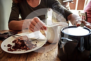 Young woman pouring cup of tea and eating cake in cafe