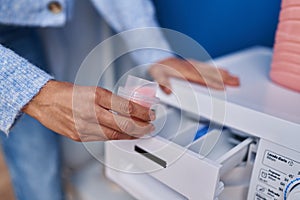 Young woman pouring detergent on washing machine at laundry room