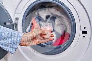 Young woman pouring detergent on washing machine at laundry room