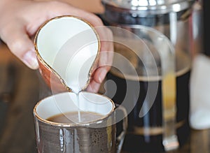 Young woman pouring milk into cup of filtered coffee