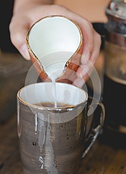 Young woman pouring milk into cup of filtered coffee