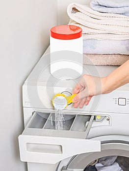 Young woman pouring washing powder into the washing machine with yellow spoon