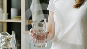 Young woman pouring water from jug into glass in the kitchen. Attractive girl drinking water on domestic kitchen.