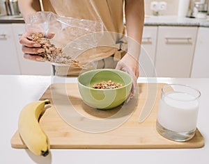 young woman pours granola into a plate for breakfast.