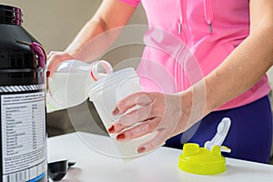 A young woman pours milk for a cocktail into a shaker. The concept of health and recovery after physical exertion